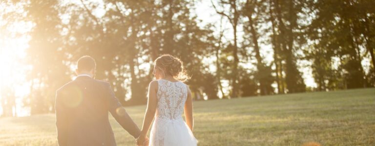 Cover image for the article called wedding expenses you can avoid. This is a bride and groom walking through a field at sunset