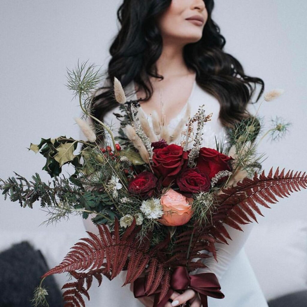 A wedding bouquet with a Christmas-theme. Dark red flowers and lots of greenery