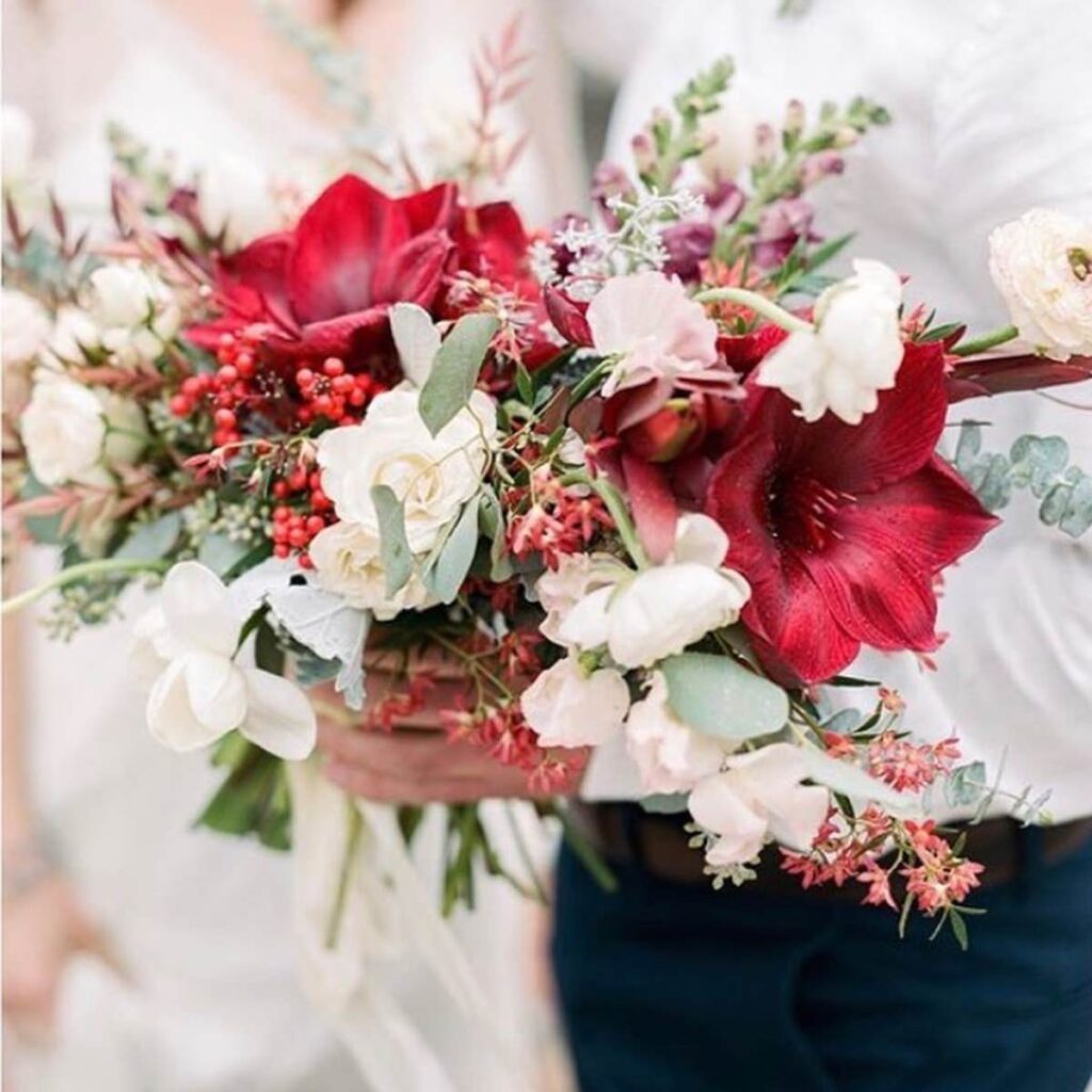 A closeup photo of a wedding bouquet with red and white flowers and pretty greenery