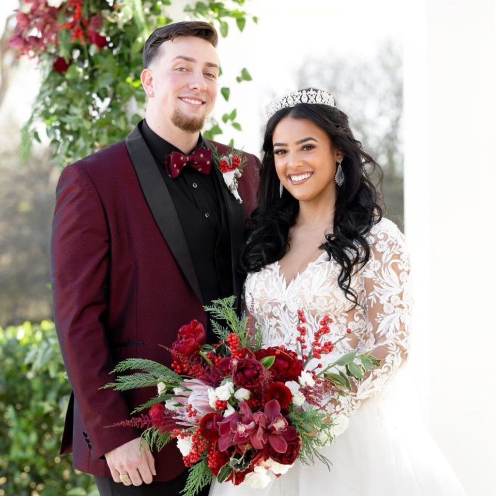 A bride and groom posing. The bride is holding a big red wedding bouquet