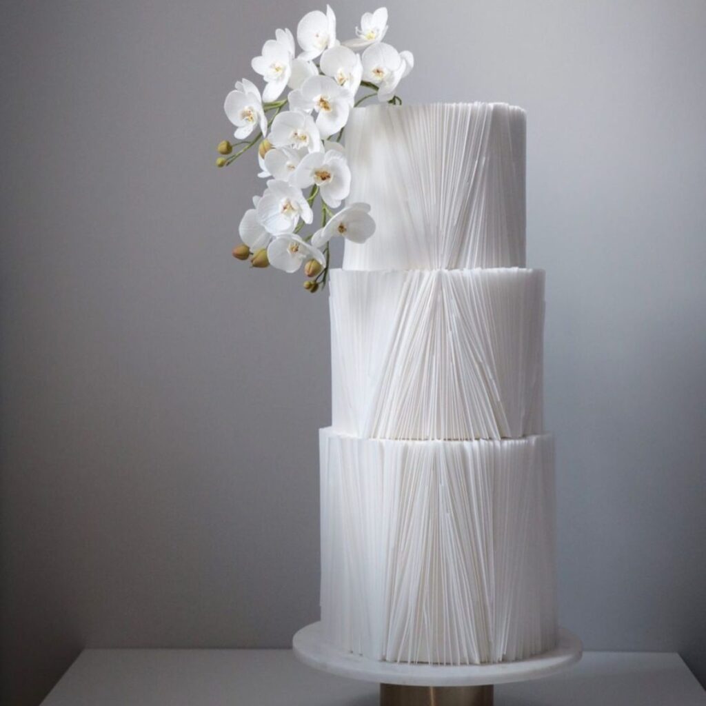 A modern 3-tier white winter wedding cake with orchids and texture
