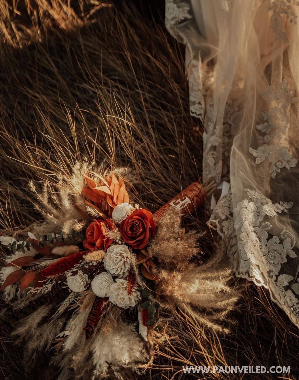 A red, brown and beige rustic bridal bouquet sitting on the ground next to the wedding dress train.