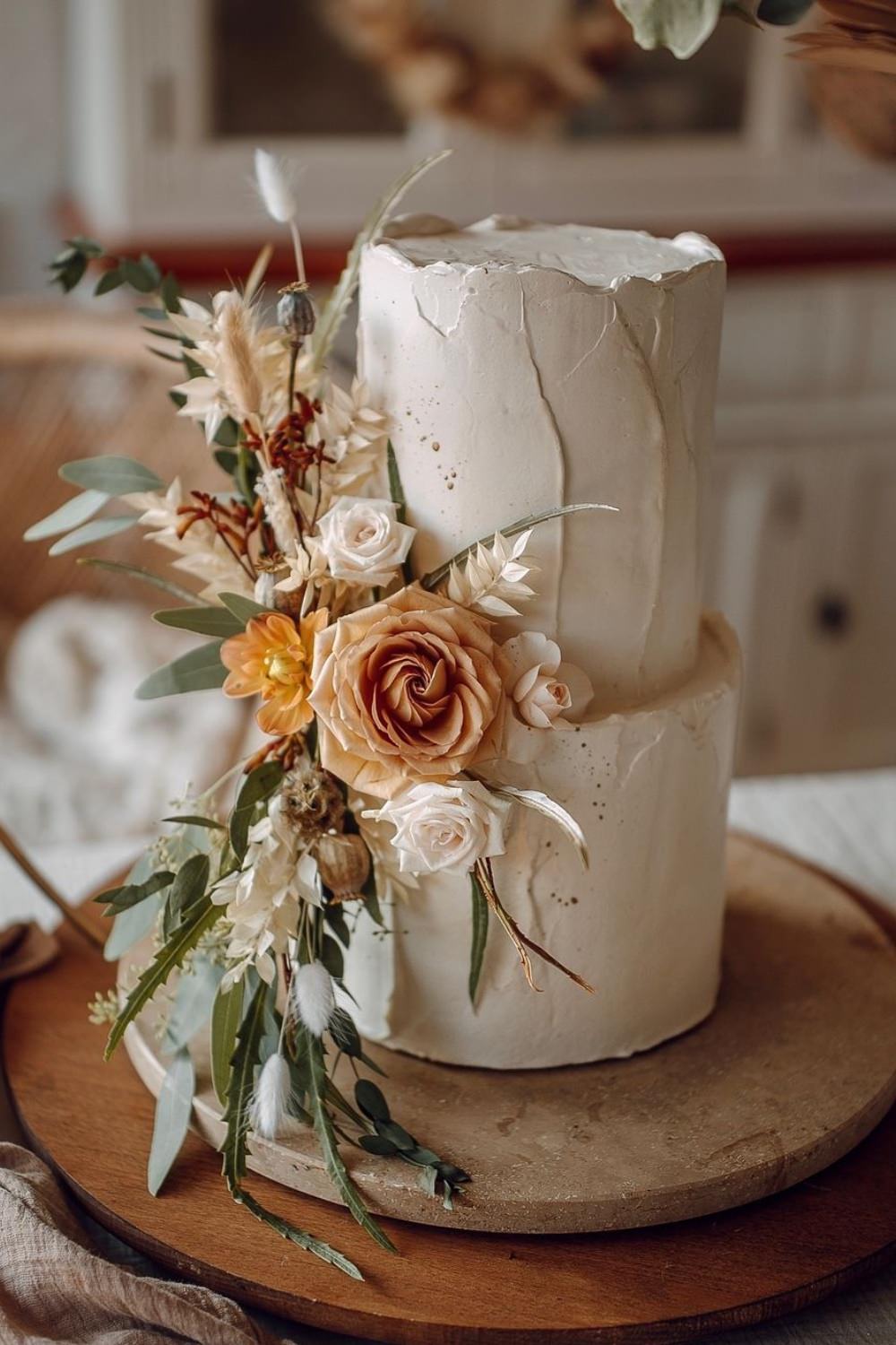 A gorgeous two-tier white wedding cake with boho style flowers
