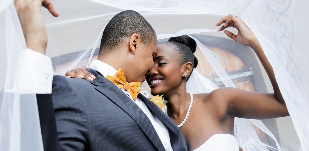A bride and groom holding up the bridal veil and smiling at each other