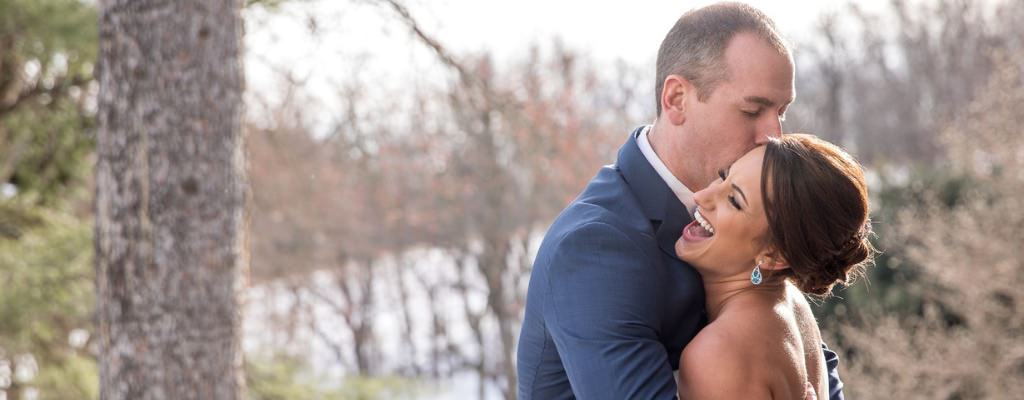 A bride laughing as the groom kisses her on the cheek