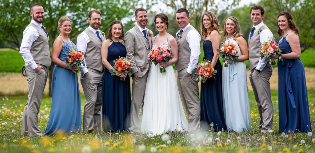 A bride and groom posing with the wedding party in a field of flowers