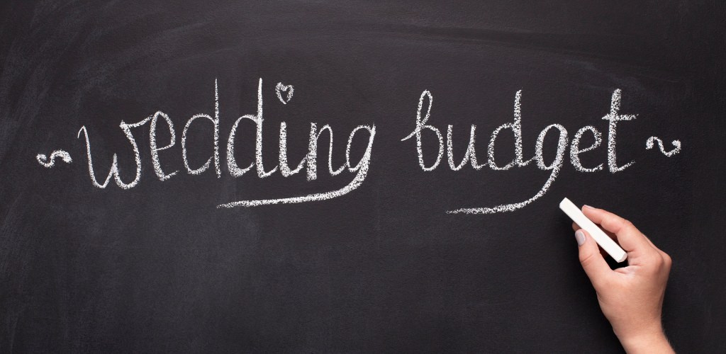 A hand writing the words wedding budget on a chalkboard
