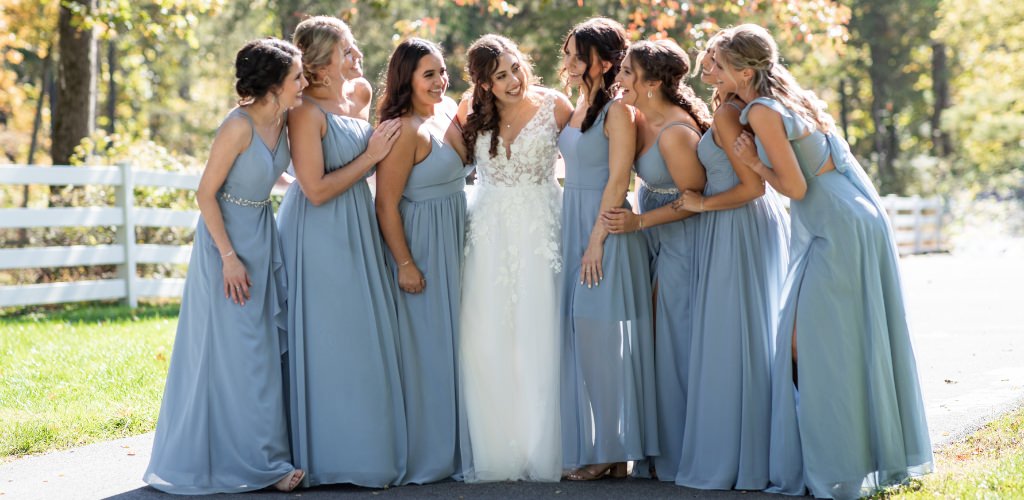A bride and bridesmaids posing and looking at each other. The girls are wearing dusty blue bridesmaid dresses