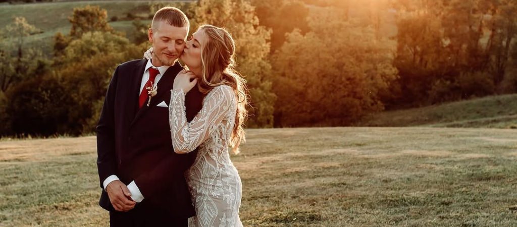 A bride kissing a groom on the cheek at sunset