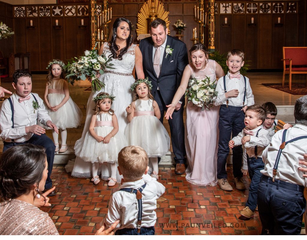 A funny and chaotic scene during family photos at a wedding. 10 kids either smiling or crying. 